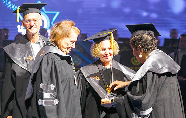 Dina Berniker (right), member of the BOT and Executive Committee, places the ceremonial hood on Agi Mishol (center) as poet Meron Isaacson and CFBIU National President Gabi Weisfeld look on