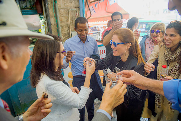 The group raises their shot glasses at one stop in the heart of Machane Yehuda. Pictured is Dr. Merav Galili (center), Vice President for Development